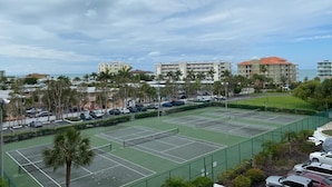 A tennis court with multiple courts, surrounded by parked cars and palm trees.