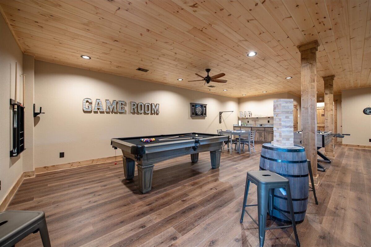A pool table in a room with wooden floors and a ceiling fan.