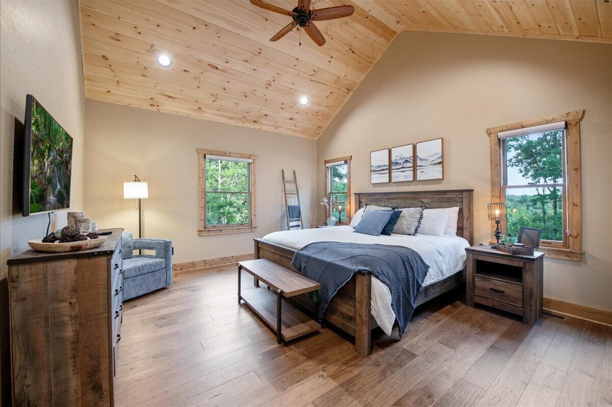 Une chambre avec un plafond en bois, de grandes fenêtres, un lit avec des oreillers, une table de chevet, une chaise et une lampe.