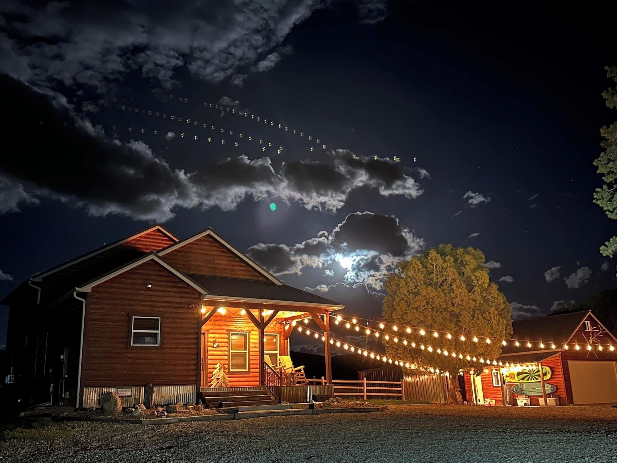 Une cabane en bois dotée d’un porche et décorée de guirlandes lumineuses, entourée d’une allée en gravier.