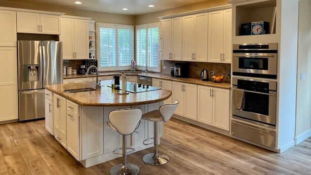A modern kitchen with white cabinets, stainless steel appliances, a central island with bar stools, and a built-in oven.