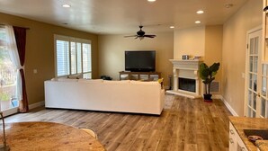 A spacious living area with a white sofa, a flat-screen TV, a fireplace, and a ceiling fan.