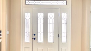 A white front door with stained glass panels, a wooden floor, and a hexagonal rug.