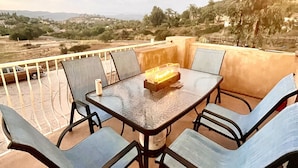 A terrace with a table and chairs, overlooking a landscape with trees and distant hills.