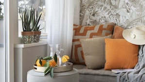 Ein gemütliches Wohnzimmer mit einer Couch, einem Beistelltisch mit Topfpflanze und Obst, und einer Wand mit Muster.