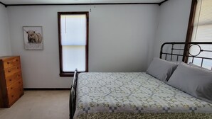 Quarto com uma cama, penteadeira de madeira, janela e um quadro na parede.