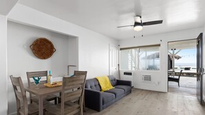 A modern living room with a dining table, wooden chairs, a grey sofa, and a ceiling fan.