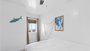 A bedroom with a bed, a window with curtains, a wall-mounted fish decoration, and a framed botanical illustration.