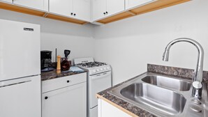 A compact kitchen with white cabinets, a gas stove, a sink, and a refrigerator. - Lower Level Pet Friendly Oceanfront Studio P925-3 (Oceanside)