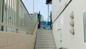 A narrow stairway leading to a building with a white exterior, a metal railing on one side, and a utility box on the ground. - Lower Level Pet Friendly Oceanfront Studio P925-3 (Oceanside)