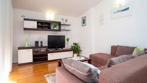 Ein modernes Wohnzimmer mit Flachbildfernseher, Holzboden und einem braunen Sofagarnitur.