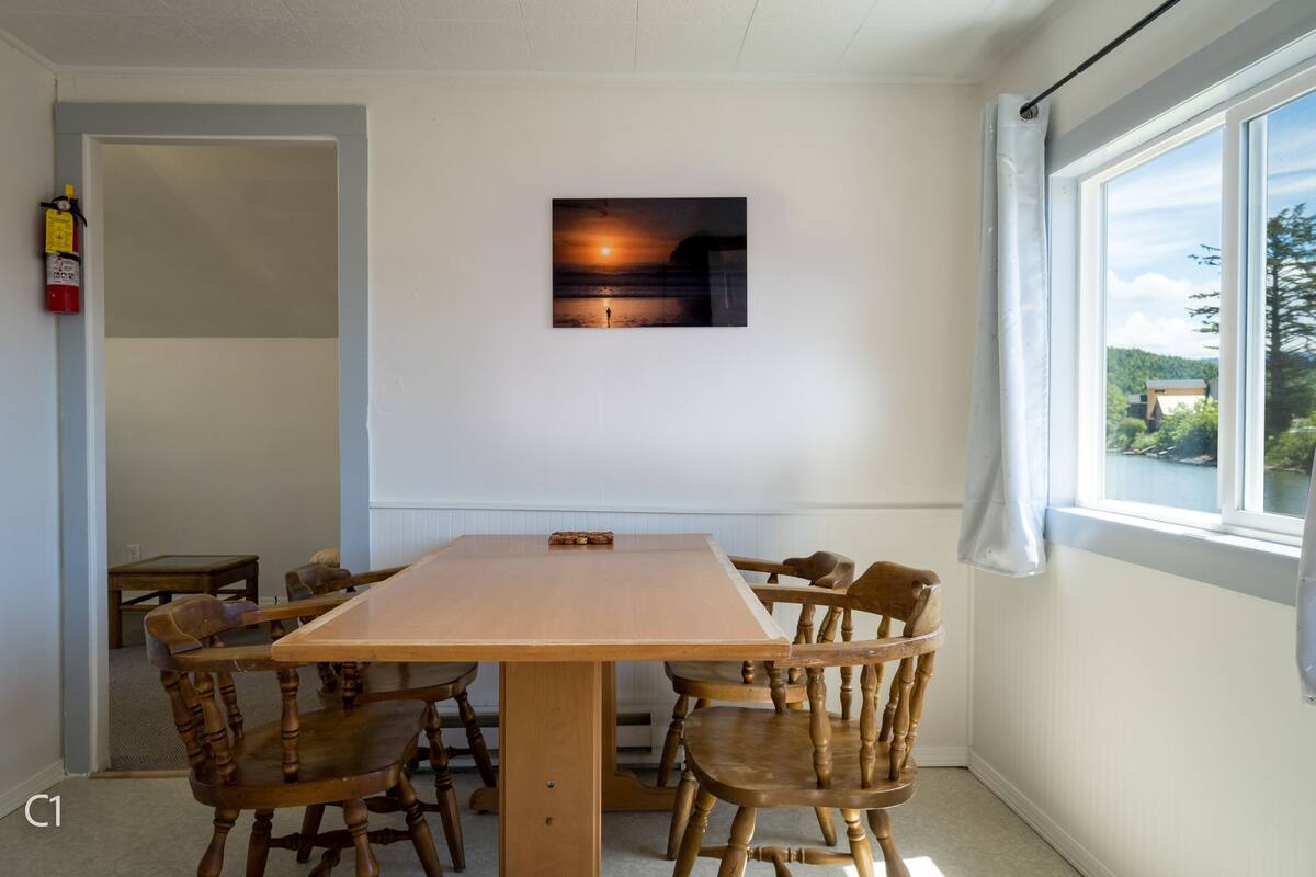 A dining area with a wooden table and chairs, a fire extinguisher on the wall, and a window with a view of the outdoors.