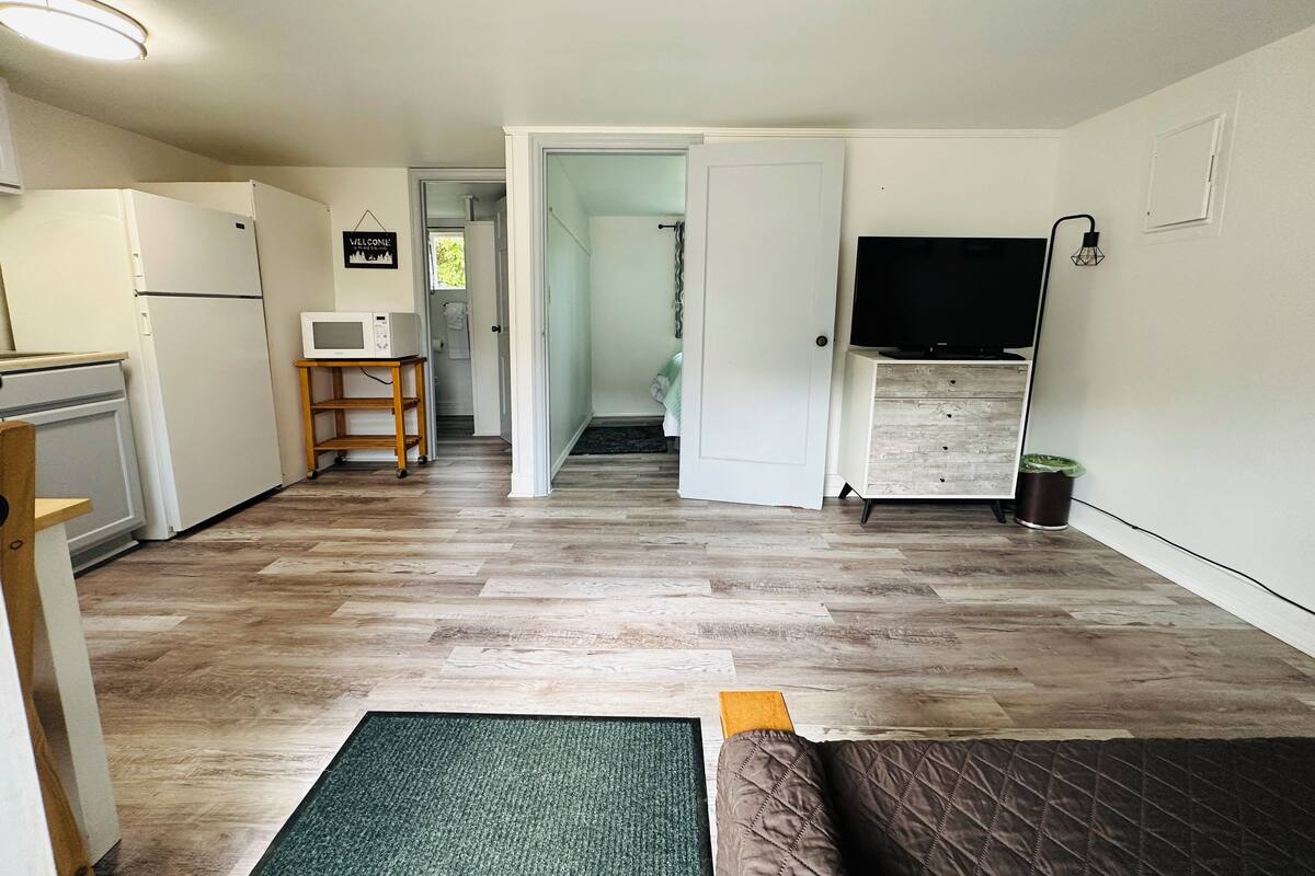 A compact living space with a kitchenette, a flat-screen TV, and a door leading to a bathroom.