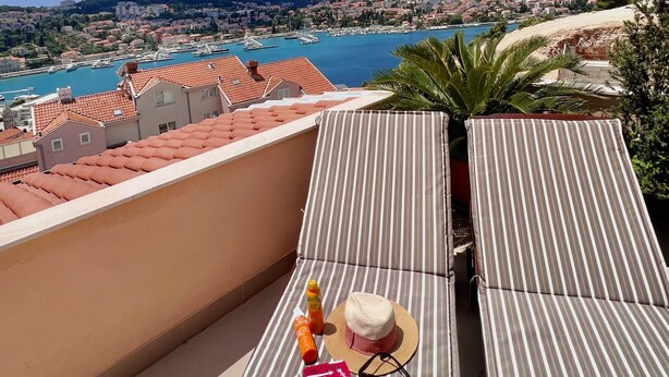 A rooftop terrace with a view of a coastal town, a hat, sunglasses, a book, and a bottle. - Apartment Lana - Two Bedroom Apartment with Terrace and Sea View (Dubrovnik)