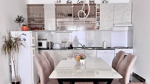 A modern kitchen with a dining area, featuring a white refrigerator, microwave, stove, and cabinets. - Apartment Lana - Two Bedroom Apartment with Terrace and Sea View (Dubrovnik)