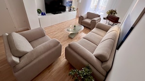A modern living room with a flat-screen TV, beige sofas, a glass coffee table, and a white cabinet. - Apartment Lana - Two Bedroom Apartment with Terrace and Sea View (Dubrovnik)