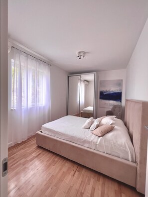 Un dormitorio con una cama grande, un espejo, un cuadro y una ventana con cortinas.