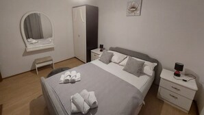 Quarto bem organizado com cama, mesas de cabeceira, guarda-roupa, espelho e uma obra de arte na parede.