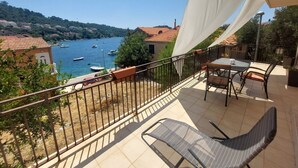 Uma varanda com mesa e cadeiras, com vista para um corpo de água onde se vêem barcos e edifícios ao fundo.