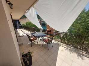A balcony with a table and chairs, a potted plant, and a view of buildings and trees. - Apartment Dominik - Two Bedroom Apartment with Terrace and Sea View (Smokvica)
