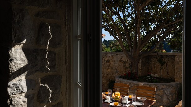 A stone wall with a wooden table set for breakfast, including plates, bowls, and glasses. - Apartment Nico's - Three Bedroom Apartment with Terrace and Sea View (Cavtat)