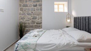 A bedroom with a stone wall, a small window, a bed with white bedding, and a bedside table with a lamp. - Apartment Nico's - Three Bedroom Apartment with Terrace and Sea View (Cavtat)