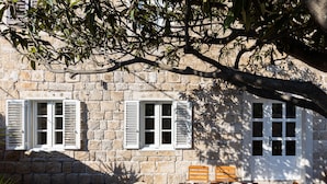 A stone building with white shutters, a table set with breakfast, and a hat on a chair. - Apartment Nico's - Three Bedroom Apartment with Terrace and Sea View (Cavtat)