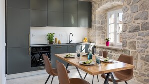 A modern kitchen with dark cabinets, a wooden dining table, and a stone wall. - Apartment Nico's - Three Bedroom Apartment with Terrace and Sea View (Cavtat)