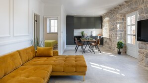 A modern living room with a mustard sofa, a dining area with a table and chairs, and a kitchen with stone walls. - Apartment Nico's - Three Bedroom Apartment with Terrace and Sea View (Cavtat)