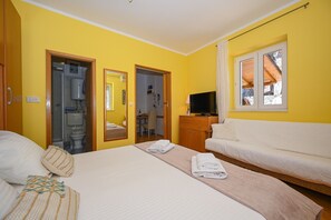 A hotel room with a bed, a sofa, a TV, and a bathroom visible through an open door.