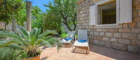 A stone building with a window and a door, two lounge chairs, and a large potted plant.