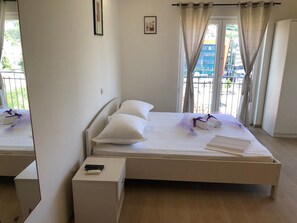 Une chambre d’hôtel moderne, équipée d’un lit, d’une table de chevet avec une télécommande et offrant une vue sur la ville grâce à de grandes fenêtres.