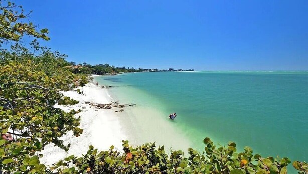Een strand met helder turquoise water en wit zand, omgeven door groen.