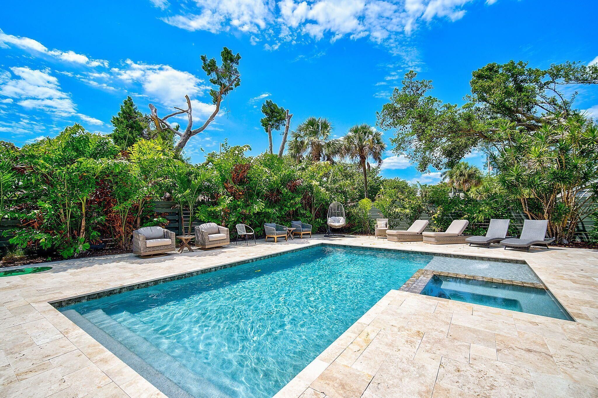 A rectangular swimming pool with a tiled deck, surrounded by lounge chairs and a variety of trees.