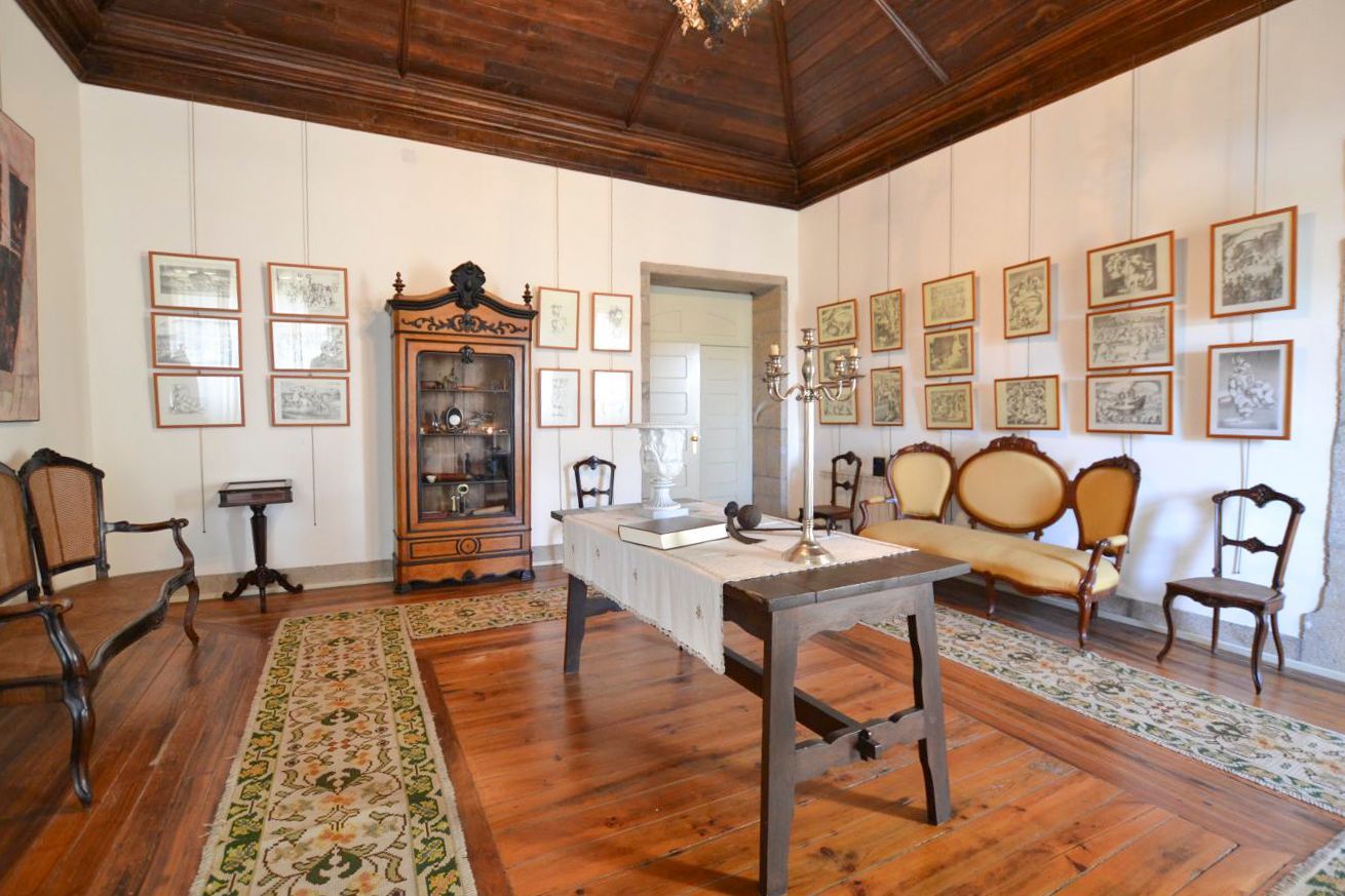 Quarto com piso de madeira, sofá, mesa e aparador com quadros nas paredes.
