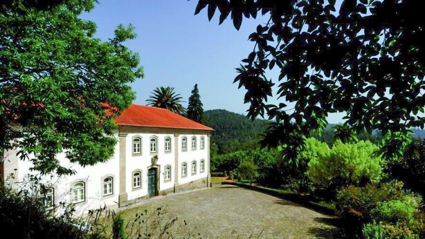 Un bâtiment blanc surmonté d’un toit rouge, entouré d’une végétation luxuriante et d’une cour pavée.