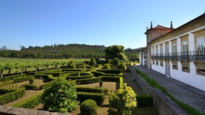 Un jardin à la française, avec des haies aux formes géométriques et un vignoble, situé à côté d’un bâtiment de style classique, doté d’une façade blanche et d’un toit rouge.