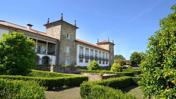 Un bâtiment historique doté d’une tour centrale, entouré de jardins magnifiquement entretenus et surplombé d’un ciel d’un bleu éclatant.