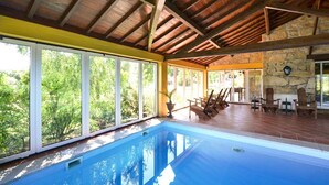 Une piscine dotée d’un plafond en bois et de grandes fenêtres donnant sur un espace verdoyant.