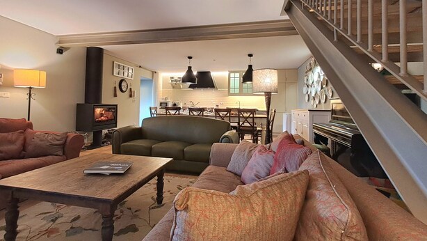 A cozy living room with a fireplace, a staircase, and a kitchen in the background.