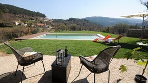 A pool area with a view of hills, two wicker chairs, and a table with a lantern.