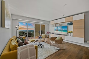 Un salon moderne avec un canapé, des fauteuils, un téléviseur et une vue sur l’extérieur.