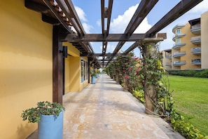 A corridor with a wooden pergola, potted plants, and a view of a building with balconies.