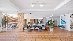 Een ruime lobby met betegelde vloer, een zithoek met stoelen en poefs, een receptiebalie en potplanten.