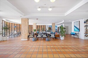 A spacious lobby with a tiled floor, seating area with chairs and ottomans, a reception desk, and potted plants. - Glamorous 2-BR Beachfront Condo w/Balcony in Aruba (Noord)