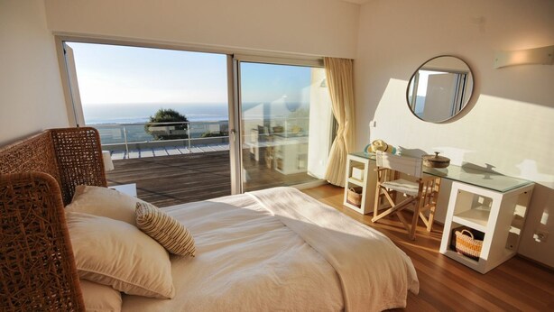 A bedroom with a large bed, a glass desk, and a view of the sea.