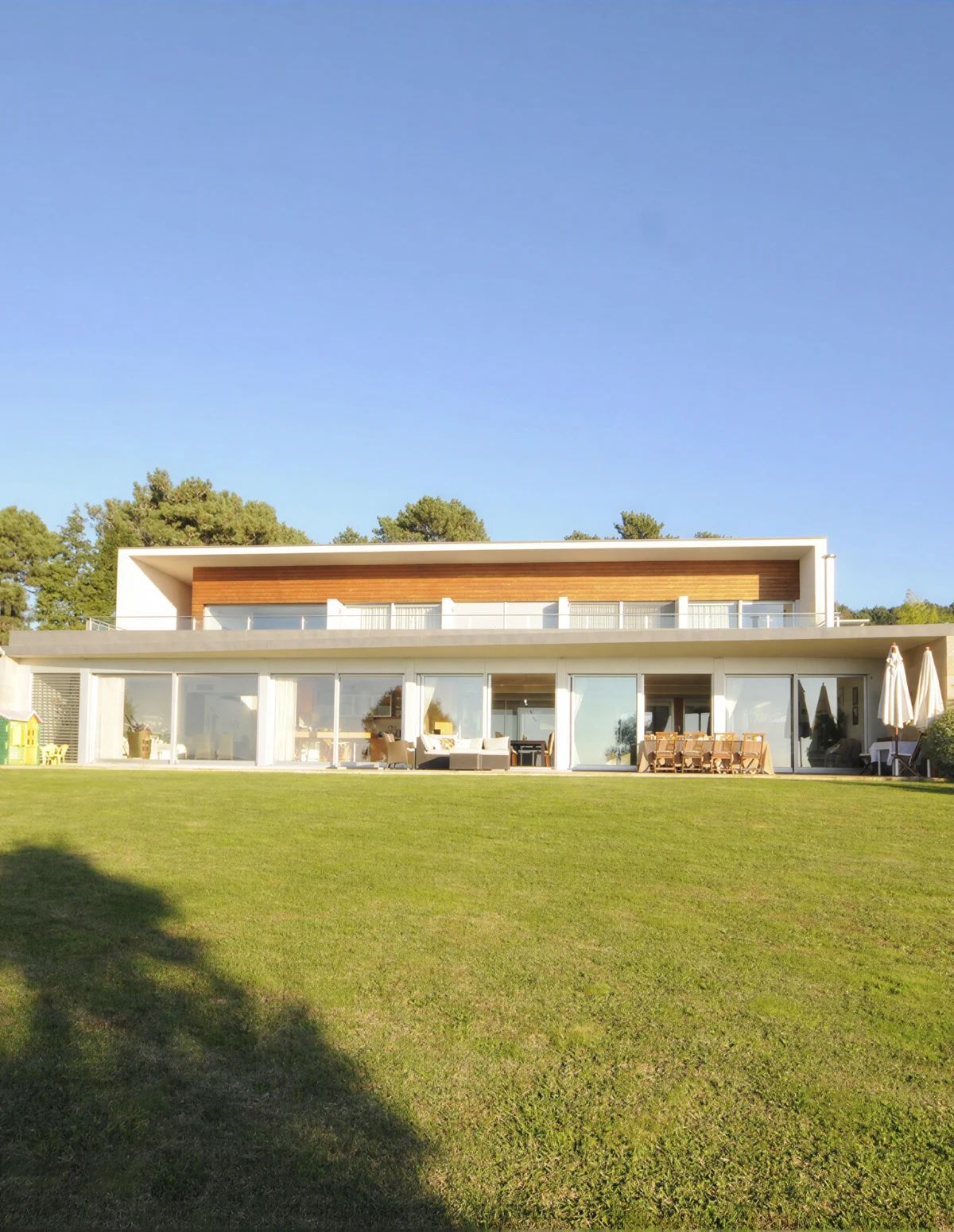 A modern two-story house with a flat roof, large glass windows, and a spacious lawn.