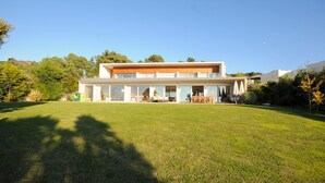 A modern two-story house with a large front lawn, a garage, and a covered outdoor seating area.