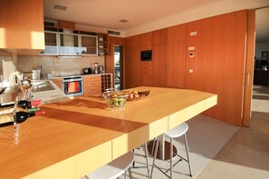 A modern kitchen with wooden cabinets, a central island with stools, and a built-in oven. - Casa Couto - Four Bedroom Villa, Sleeps 8 (Caminha)