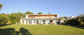 A modern two-story house with a flat roof, large windows, and a spacious front yard.